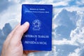 Man`s hand holding Brazilian Work Card on blue sky and clouds background. Written in Portuguese Federative Republic of