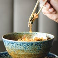 Man`s hand holding chopsticks over a plate of Japanese, thai, chinese meal - rice, mushroom, vegetables. Cafe Royalty Free Stock Photo