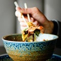 Man`s hand holding chopsticks over a plate of Japanese, thai, chinese meal - rice, mushroom, vegetables. Cafe Royalty Free Stock Photo