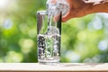 Man`s hand holding drinking water bottle water and pouring water into glass on wooden tabletop on blurred green bokeh background