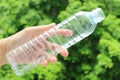 Man`s hand holding an empty plastic bottle of drinking water against blurry green foliage Royalty Free Stock Photo