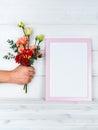 Man`s hand holding flowers and a photo frame on wooden background.