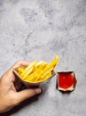 Man`s hand holding french fries in the brown paper wrapper with sauce isolated with abstract background. with copy space Royalty Free Stock Photo