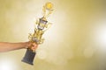 Man`s hand holding golden winner trophy cup on blurred golden bokeh background