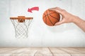 Man`s hand holding orange basketball ready to throw it into basketball hoop fixed on grungy white wall with red painted