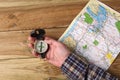 Man`s hand holding an orientation compass on a wooden table with a map and copy space for your text Royalty Free Stock Photo