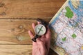 Man`s hand holding an orientation compass on a wooden table with a map and copy space for your text Royalty Free Stock Photo