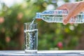 Man`s hand holding plastic bottle water and pouring water into glass on wooden table on blurred green bokeh background Royalty Free Stock Photo