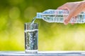 Man`s hand holding plastic bottle water and pouring water into glass on wooden table on blurred green bokeh background Royalty Free Stock Photo