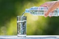 Man`s hand holding plastic bottle water and pouring water into glass on wooden table on blurred green bokeh background Royalty Free Stock Photo