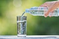 Man`s hand holding plastic bottle water and pouring water into glass on wooden table on blurred green bokeh background Royalty Free Stock Photo