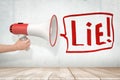 Man`s hand holding red and white megaphone against grungy white wall with big speech bubble that says `Lie`