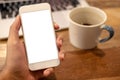 A man`s hand holding white mobile phone with blank desktop screen with coffee cup and laptop on wooden table Royalty Free Stock Photo