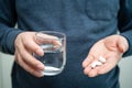 A man`s hand holding a white pill and a cup of water in hand Royalty Free Stock Photo