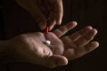 A man`s hand holding a white pill. Hand holding a red capsule. on black background. Free space to write. Drug for legal use Royalty Free Stock Photo