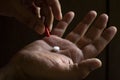 A man`s hand holding a white pill. Hand holding a red capsule. on black background. Free space to write. Drug for legal use Royalty Free Stock Photo