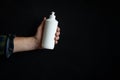 A man`s hand holding a white soap bottle on a black background. Unbranded blank bottle with liquid soap Royalty Free Stock Photo