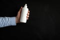 A man`s hand holding a white soap bottle on a black background. Unbranded blank bottle with liquid soap Royalty Free Stock Photo