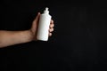 A man`s hand holding a white soap bottle on a black background. Unbranded blank bottle with liquid soap Royalty Free Stock Photo