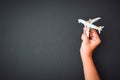 Man`s hand holding white toy airplane model over black color wall background with copy space, concept of travel Royalty Free Stock Photo