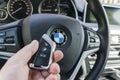 Man`s hand holding a wireless BMW X5 F15 car key in black leather interior. Modern Car interior details. Car detailing. Car inside