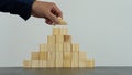 Man`s hand holding wooden block pyramid top on table and construction concept.