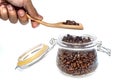 A man`s hand holding wooden spoon to scooping roasted coffee beans from glass jar in white background Royalty Free Stock Photo