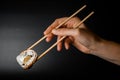 Man& x27;s hand holds bamboo chopsticks with Philadelphia sushi roll with smoked eel, salmon and cream cheese