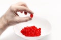 Man's hand holds a cherry over a white bowl with delicious red dried cherries. White background Royalty Free Stock Photo