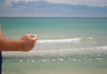 Man`s hand holds a coin from the metal eagle tails against the sea, is about to throw a coin into the sea to return