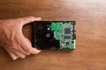 A man`s hand holds a hard disk memory located on a wooden base. The hard drive shows electronics and a printed circuit board Royalty Free Stock Photo