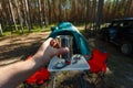 The man's hand holds an iron mug with a warm drink on the background of the table and chairs, campfire, a tent and an SUV in camp Royalty Free Stock Photo