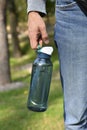 Man`s hand holds plastic reusable sports water bottle on a nature background. Concept of environmental protection, save nature, ec