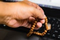 Man`s hand holds prayer beads against laptop keyboard Royalty Free Stock Photo