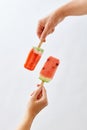 A man`s hand holds a slice of watermelon on a stick, in the form of an ice cream, and a red ice cream lolly in a woman`s Royalty Free Stock Photo