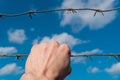 Man's hand holds stretched rusty barbed wire against blue sky with clouds. The concept of prison, crime, safety, border Royalty Free Stock Photo