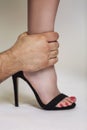 A man`s hand holds a woman`s leg. Complex relationship in a couple. Gray background. Close-up. Vertical