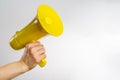 A man`s hand holds a yellow loudspeaker, megaphone. Isolated on white background. It symbolizes untrue news, rumors, fakes,