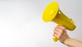 A man`s hand holds a yellow megaphone on a white background. It symbolizes rumors, fakes, false information. Elections, debates,