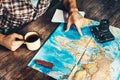 Man`s hand indicates a route on a paper map. Another hand holds a mug of tea. The man is inspired by photography and plans a hike