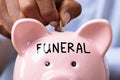 Human Hand Inserting Coin In Piggy Bank With Funeral Text