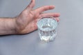 A man`s hand intends to take a glass of water. A glass of clear drinking water against a gray background