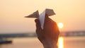 Man`s hand of launch paper plane against the sea during sunset with sun flare and reflections in the water in slowmotion Royalty Free Stock Photo