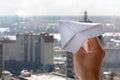 Man`s hand launches a paper airplane in a window against the background of city