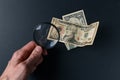 Man`s hand with magnifying glass and money on black background. Paper currency. Looking For Money Royalty Free Stock Photo