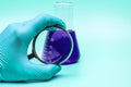 A man`s hand in medical glove holds a magnifying glass near a glass laboratory flask liquid. The concept of medical and chemical Royalty Free Stock Photo