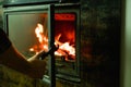 A man`s hand opens the glass door of the fireplace in which the wood is burning. Modern closed fireplace with glass