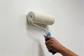 Man`s hand with a paint brush roller painting interior wall in white