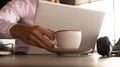 man's hand picking up a cup of coffee behind the laptop Royalty Free Stock Photo