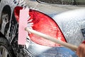 Man`s hand with pink brush washing gray car.